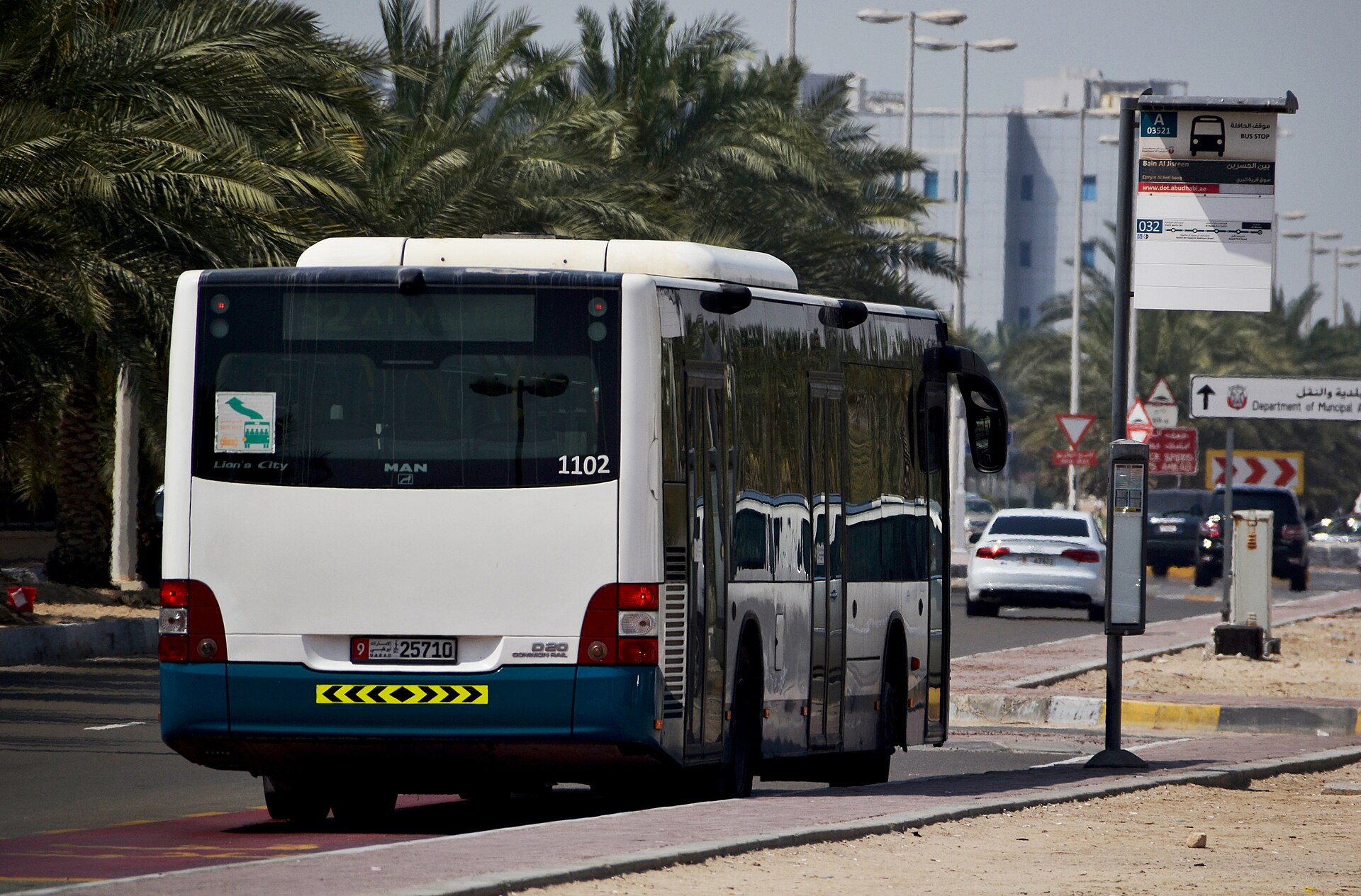 Public bus passing a marked bus-stop pavilion on a palm-lined avenue in Abu Dhabi