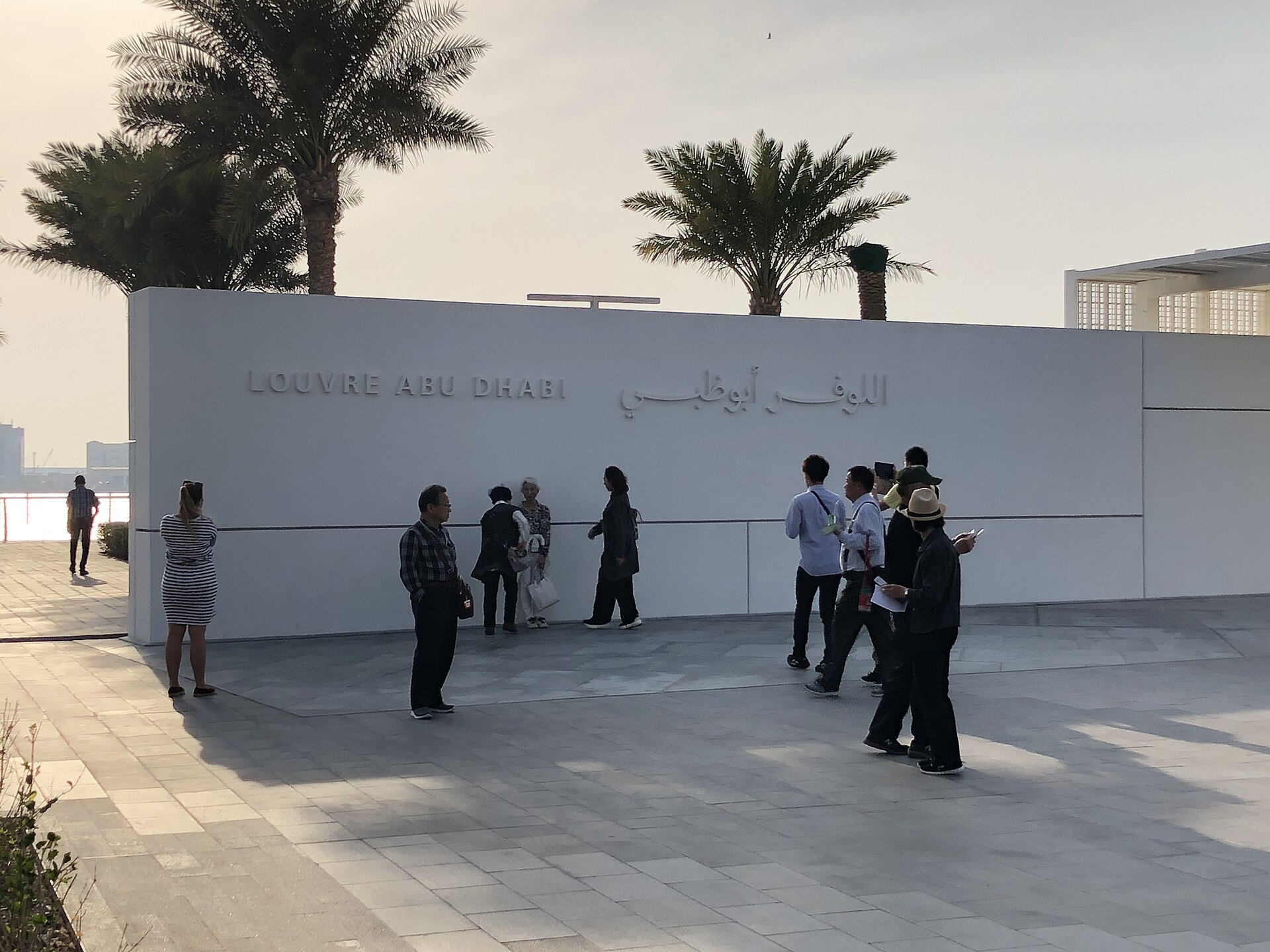 Louvre Abu Dhabi exterior wall with bilingual signage and palm trees